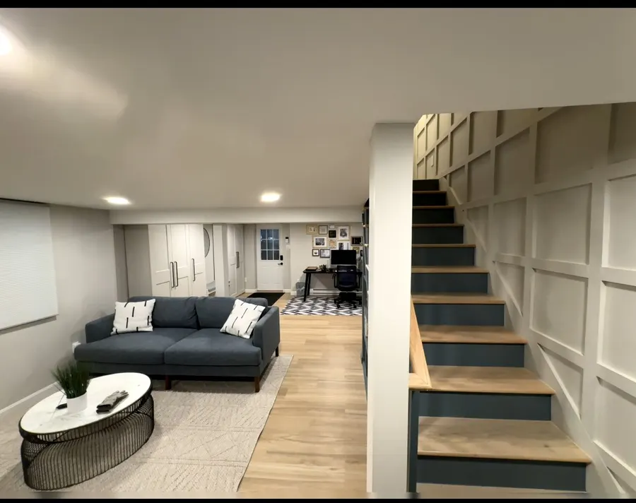 Finished basement living area with paneled staircase