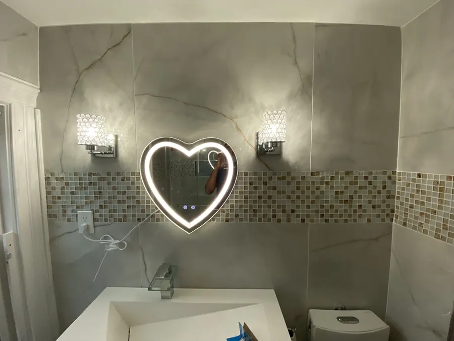 Remodeled bathroom with heart-shaped lit mirror and tile accent band