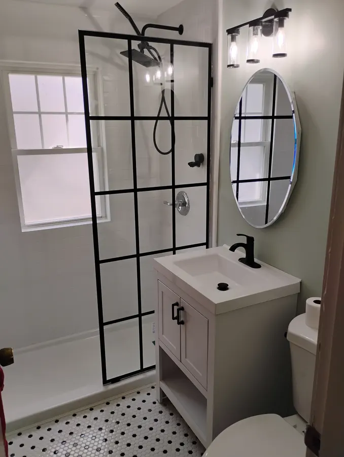 Finished bathroom with black-framed glass shower and round mirror