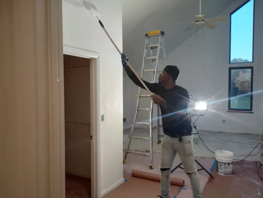 Crew member painting a ceiling with a roller on a ladder